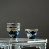 Stack of hand-painted blue and white porcelain teacups with silver trim on a wooden table.