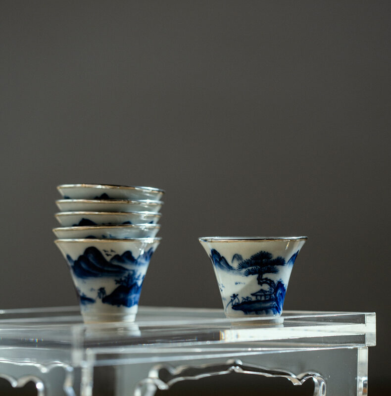 Stack of hand-painted blue and white porcelain teacups with silver trim on a wooden table.