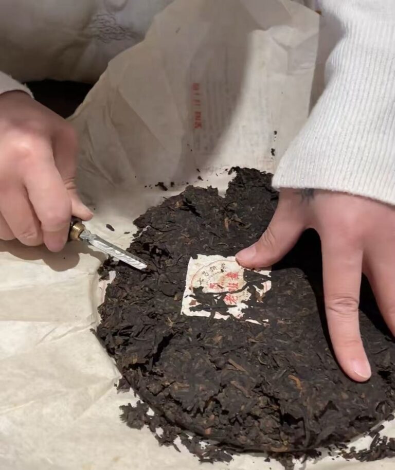 Pu Erh tea cake with a tea pick and loosened leaves for beginner cake breaking