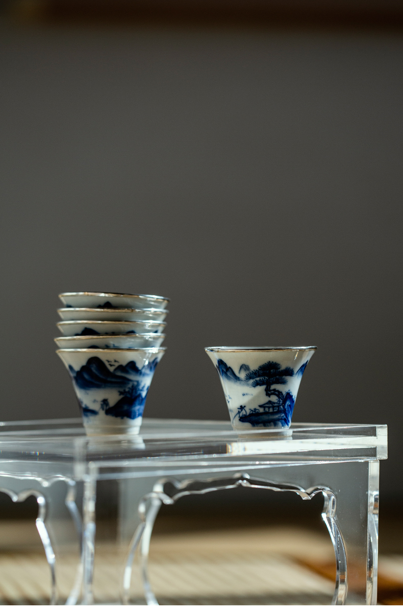 Stack of hand-painted blue and white porcelain teacups with silver trim on a wooden table.